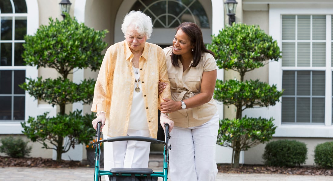 A caregiver assisting a person with a walker.