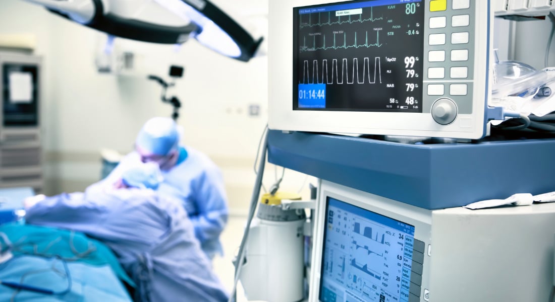 Hospital equipment, while two doctors perform surgery in the background.