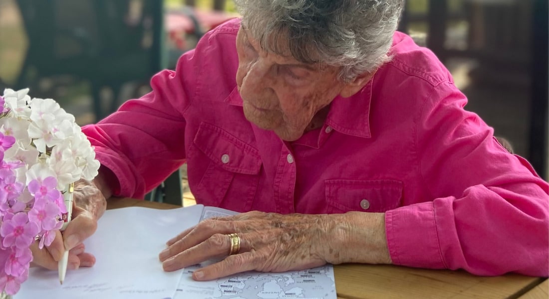 An older person sitting at a table, writing in a booklet.
