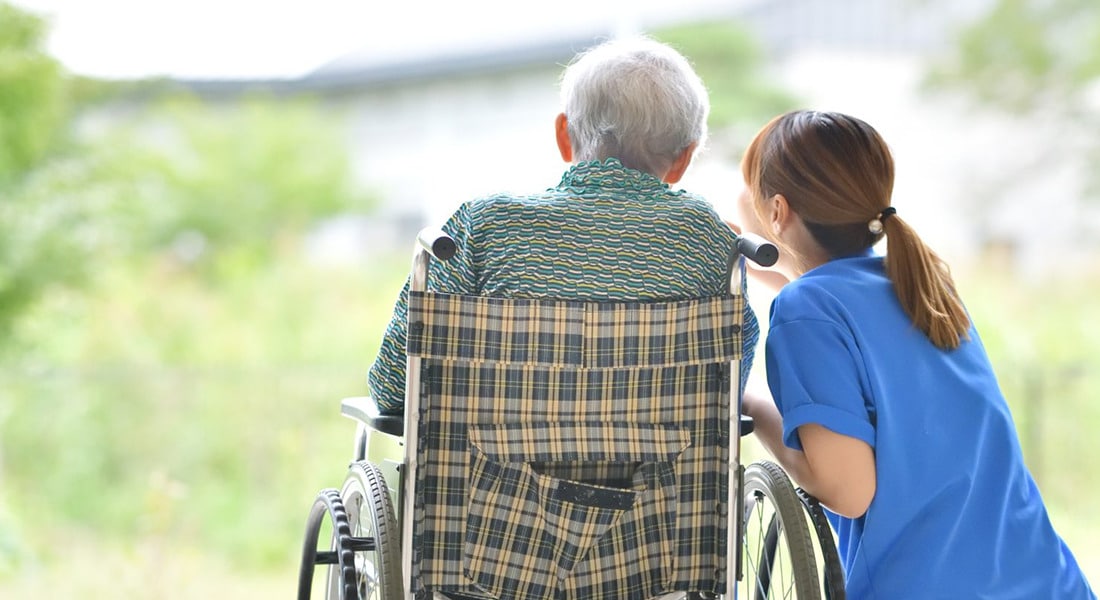 A caregiver sitting outside with a person in a wheelchair.
