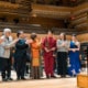 A group of people clapping for each other on stage in front of an orchestra.