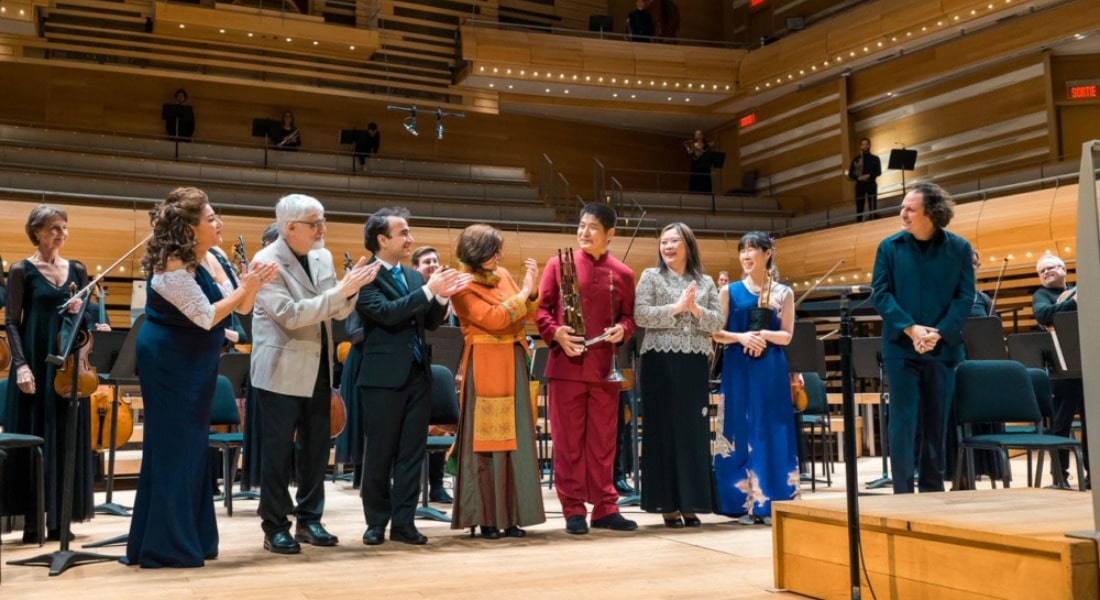A group of people clapping for each other on stage in front of an orchestra.