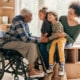 A person holding two young children while an older person in a wheelchair holds their hands.