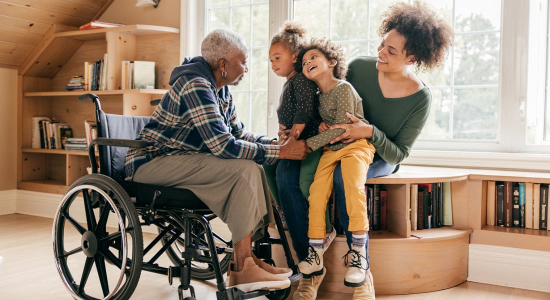 A person holding two young children while an older person in a wheelchair holds their hands.